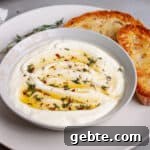 A serving bowl of whipped ricotta dip topped with honey and herbs on a plate with toasted bread.