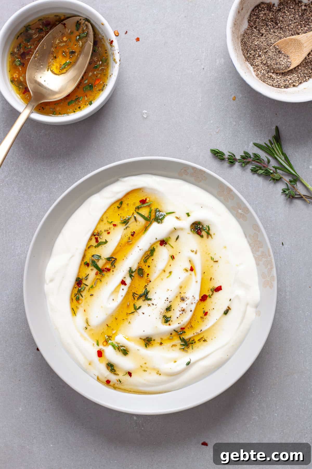 A serving bowl of whipped ricotta cheese dip topped with honey and herbs on a gray table.