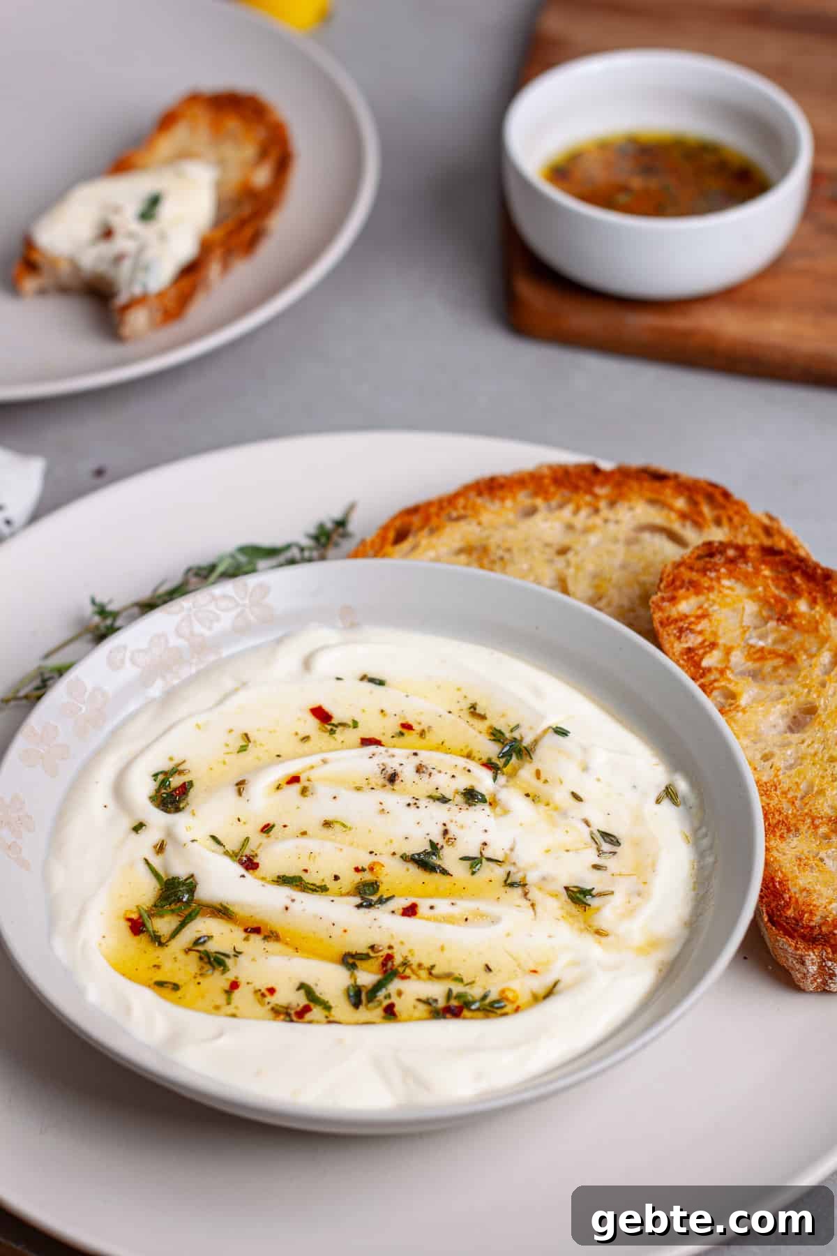 A serving bowl of whipped ricotta dip topped with honey and herbs on a plate with toasted bread.