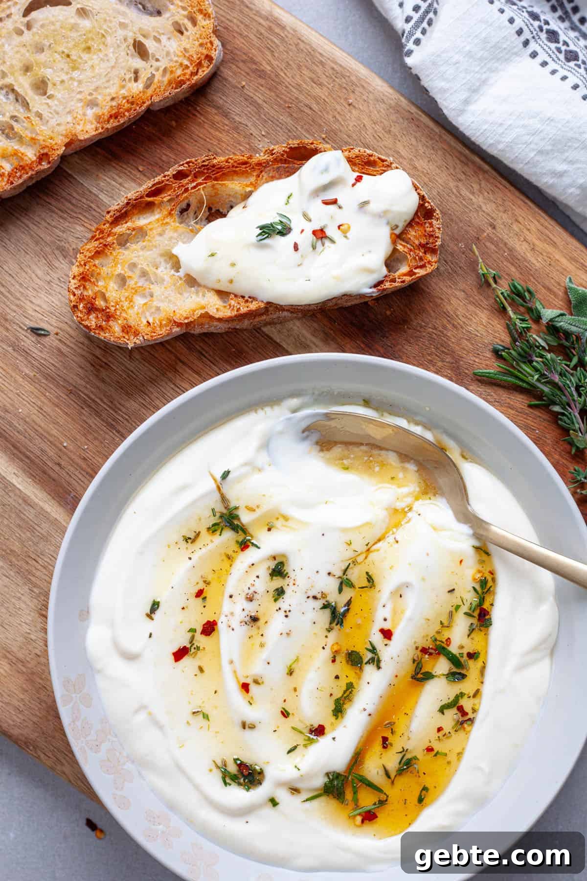 A cutting board with a piece of toast topped with whipped ricotta with a ricotta dip to the side.