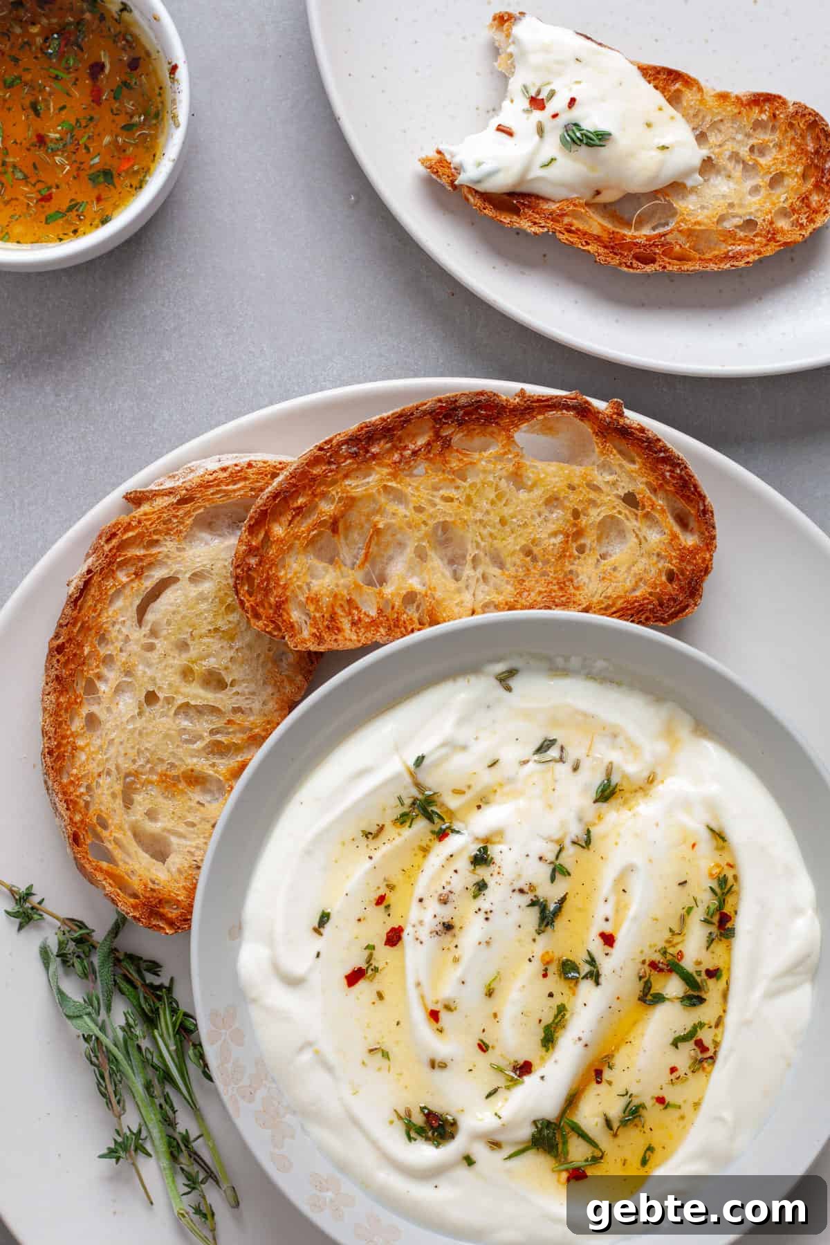 A platted of toasted bread with whipped ricotta dip topped with honey and herbs and a serving to the side.