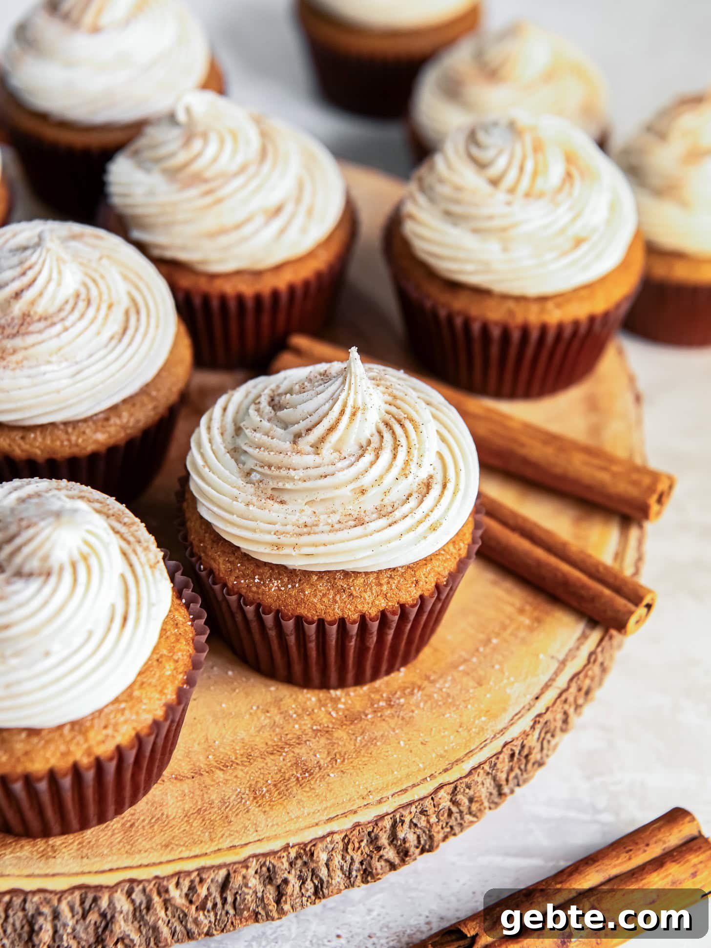 Maple Cream Cheese Frosted Spice Cupcakes 6 Frosted cupcakes on a wooden board near cinnamon sticks.