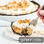 Decadent Butterfinger Pie Recipe: Chocolate-Peanut Butter Layered Pie 7 slice of pie on a plate with the rest of the pie in the background and a hand reaching in with a fork to take a bite
