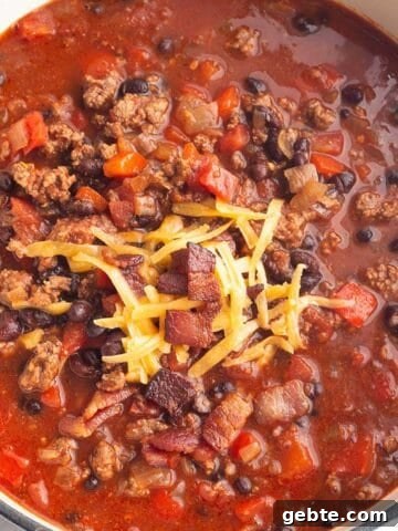 A white Dutch Oven full of a chili made with ground beef, black beans and bacon.