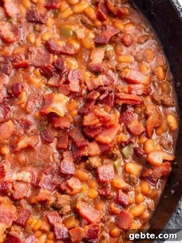 A cast iron pan with a baked bean dish topped with crispy bacon.