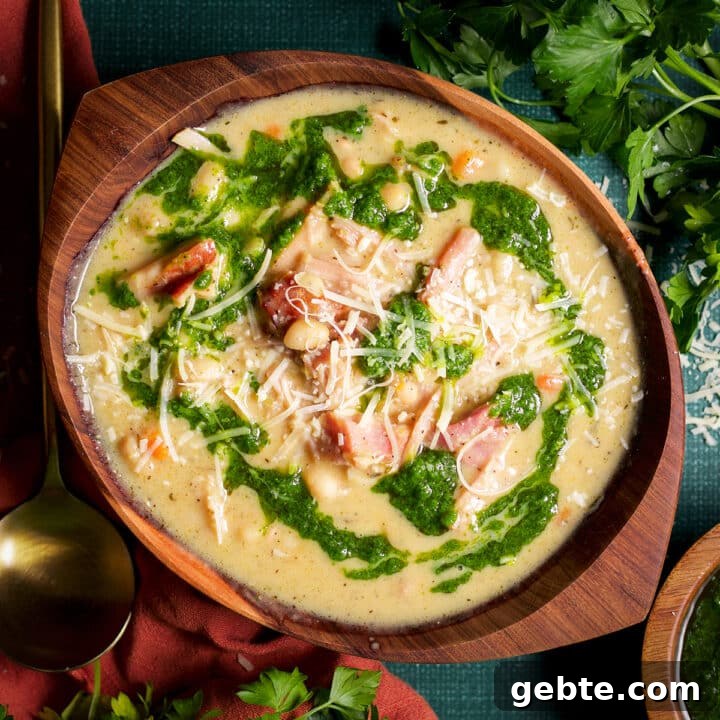 A bowl of navy bean soup with ham topped with herb oil and shredded parmesan cheese.