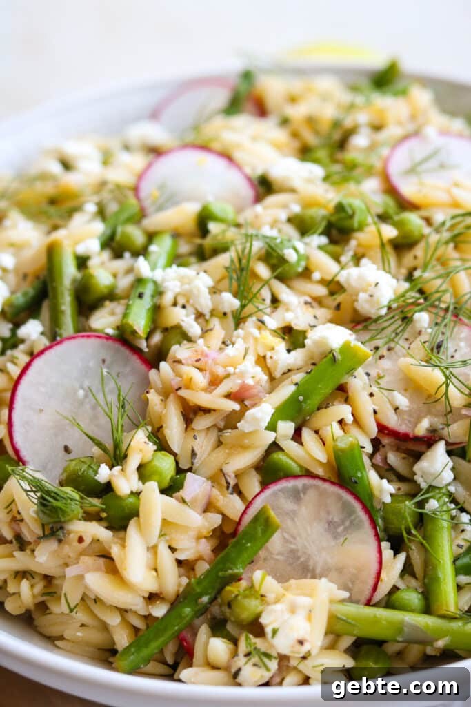 orzo salad with asparagus and peas in white bowl with lemons in the background