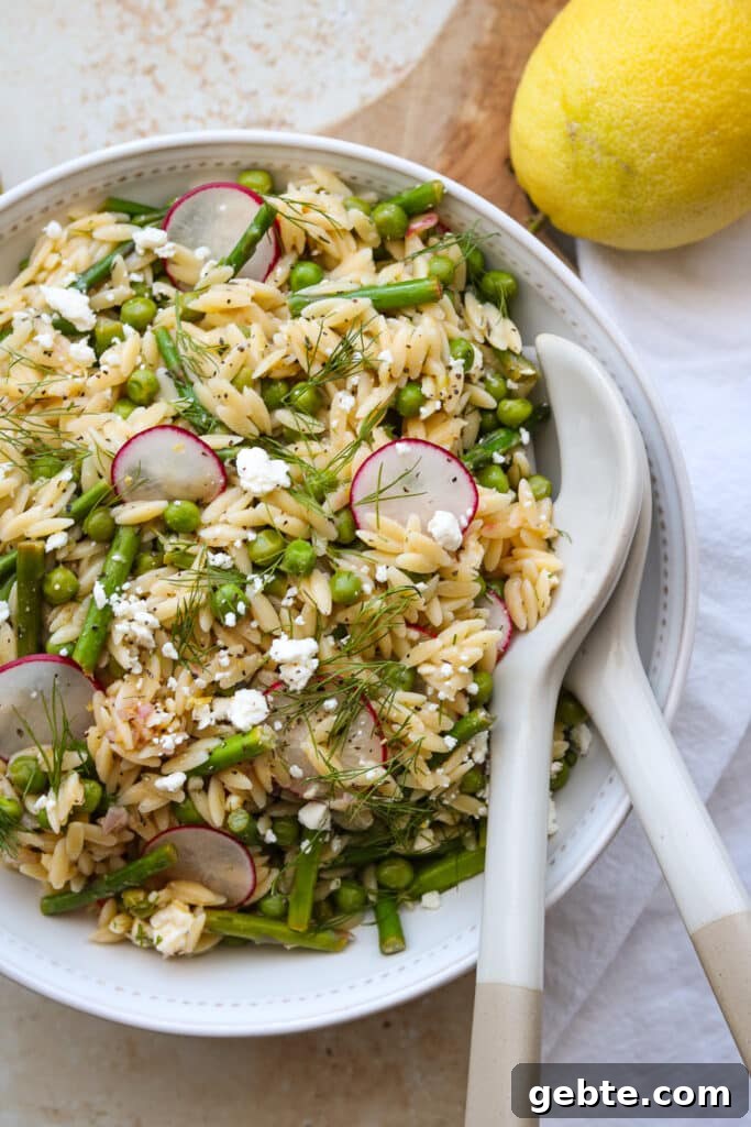 orzo salad with asparagus and peas in white bowl with serving utensils and lemon 