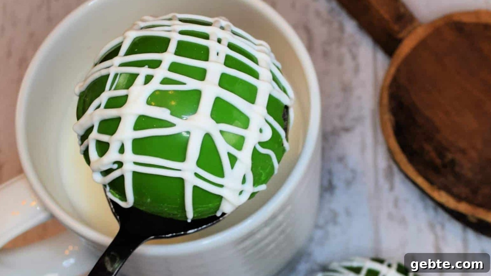 St. Patrick's Day Hot Chocolate Cocoa Bomb with white icing drizzle, resting on a spoon over a white cup.