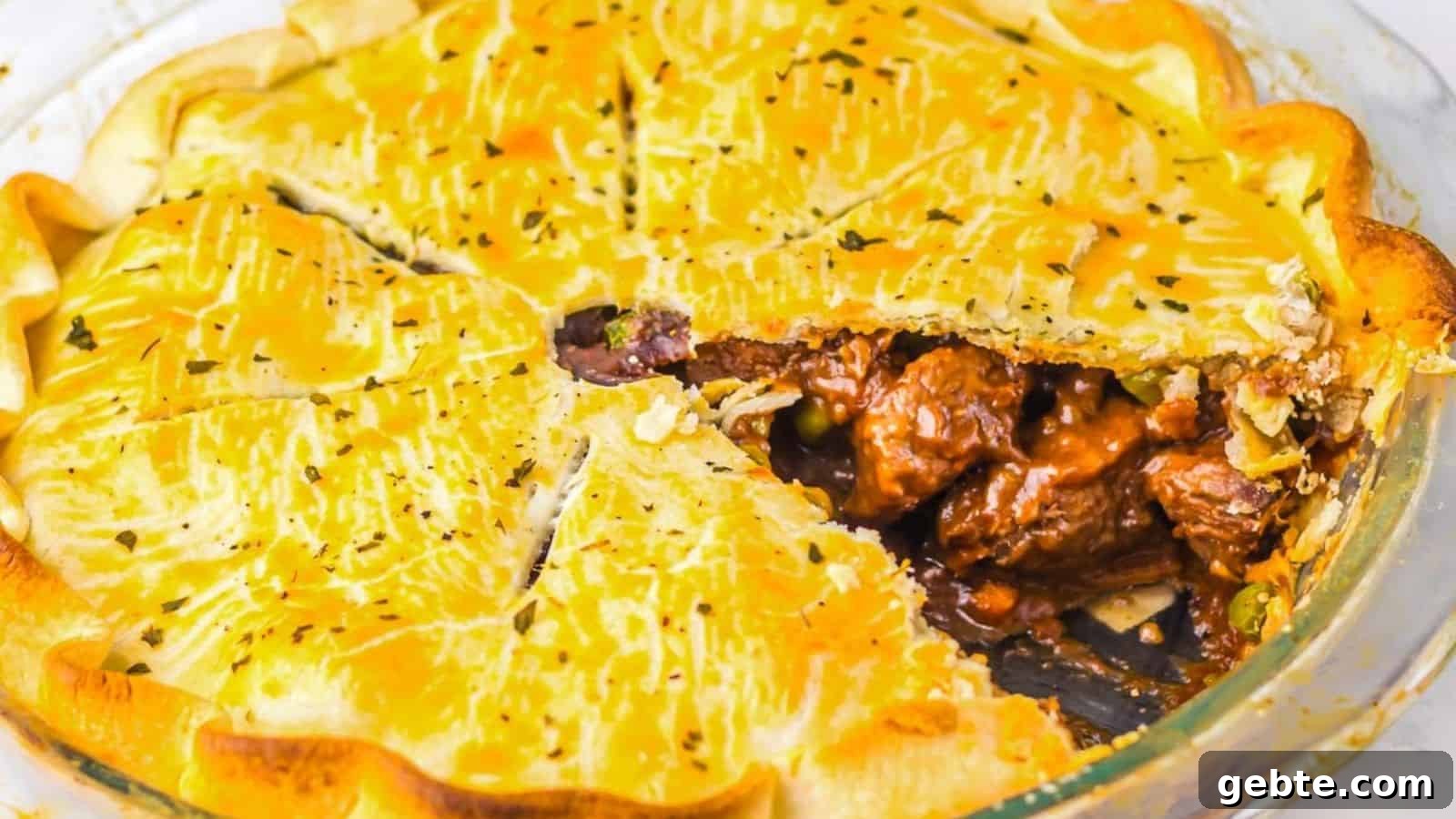 A close-up of a beef and vegetable pie with a golden, flaky crust. A triangular segment is removed, revealing chunks of beef and vegetables in a savory sauce inside the pie. The crust is lightly seasoned with herbs.