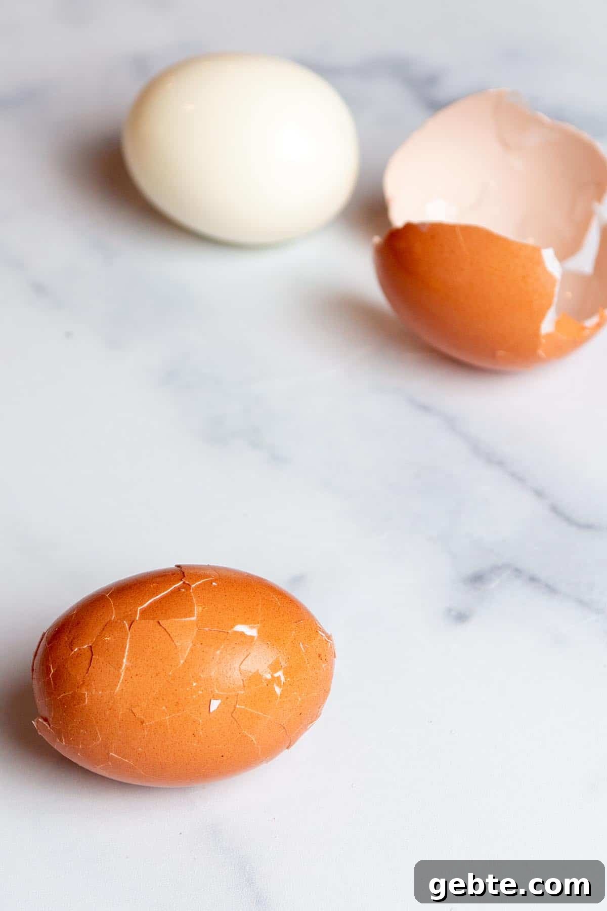 Two eggs one with cracks in the shell and one out of its shell.