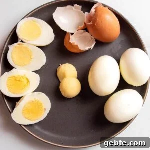 A plate with hard boiled eggs one peeled, one cut in half and one with the yolks removed.