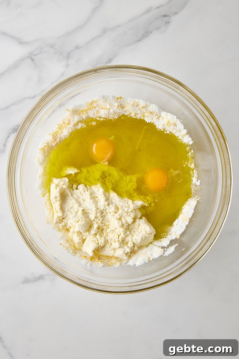 Lemon olive oil, ricotta, eggs, lemon juice, and lemon-sugar in glass bowl