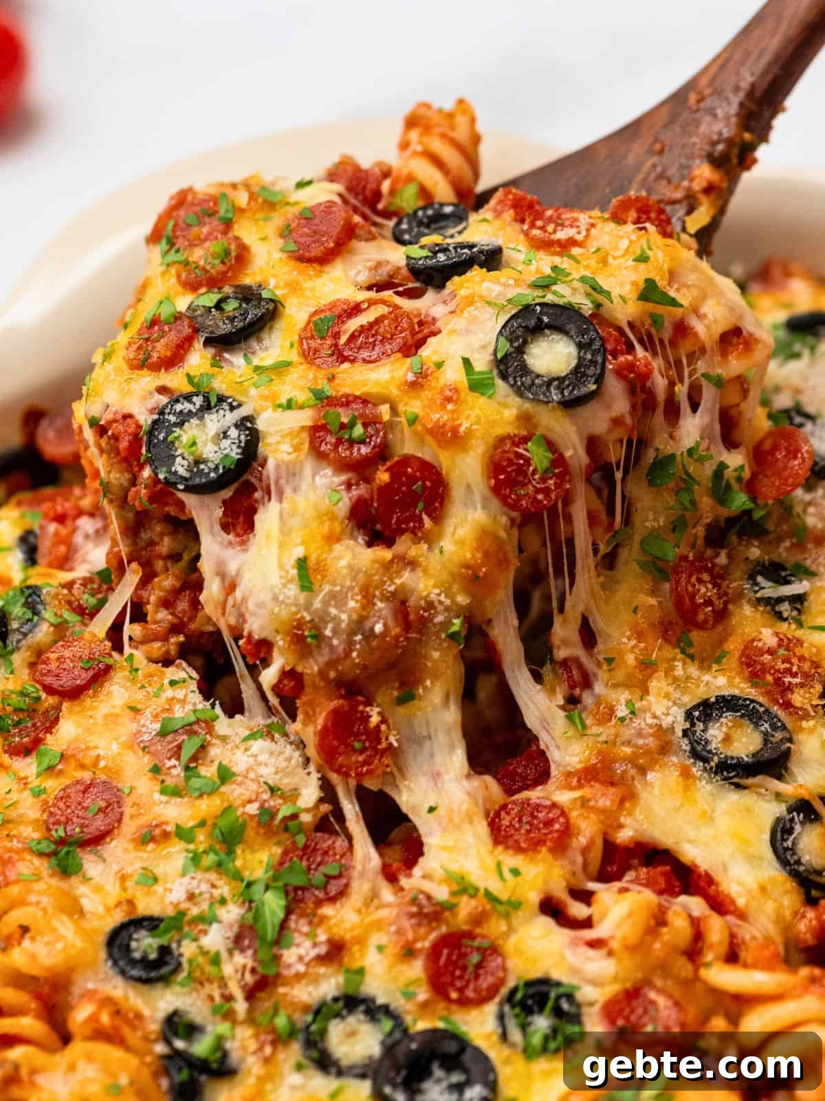 Spoonful of cheesy pasta bake with pizza sauce, pepperoni, and olives.