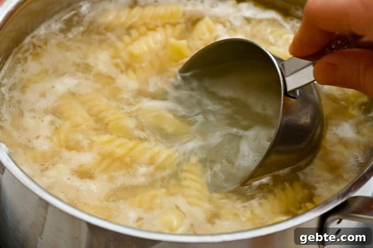 A measuring cup scooping out a bit of pasta water from boiling rotini noodles.