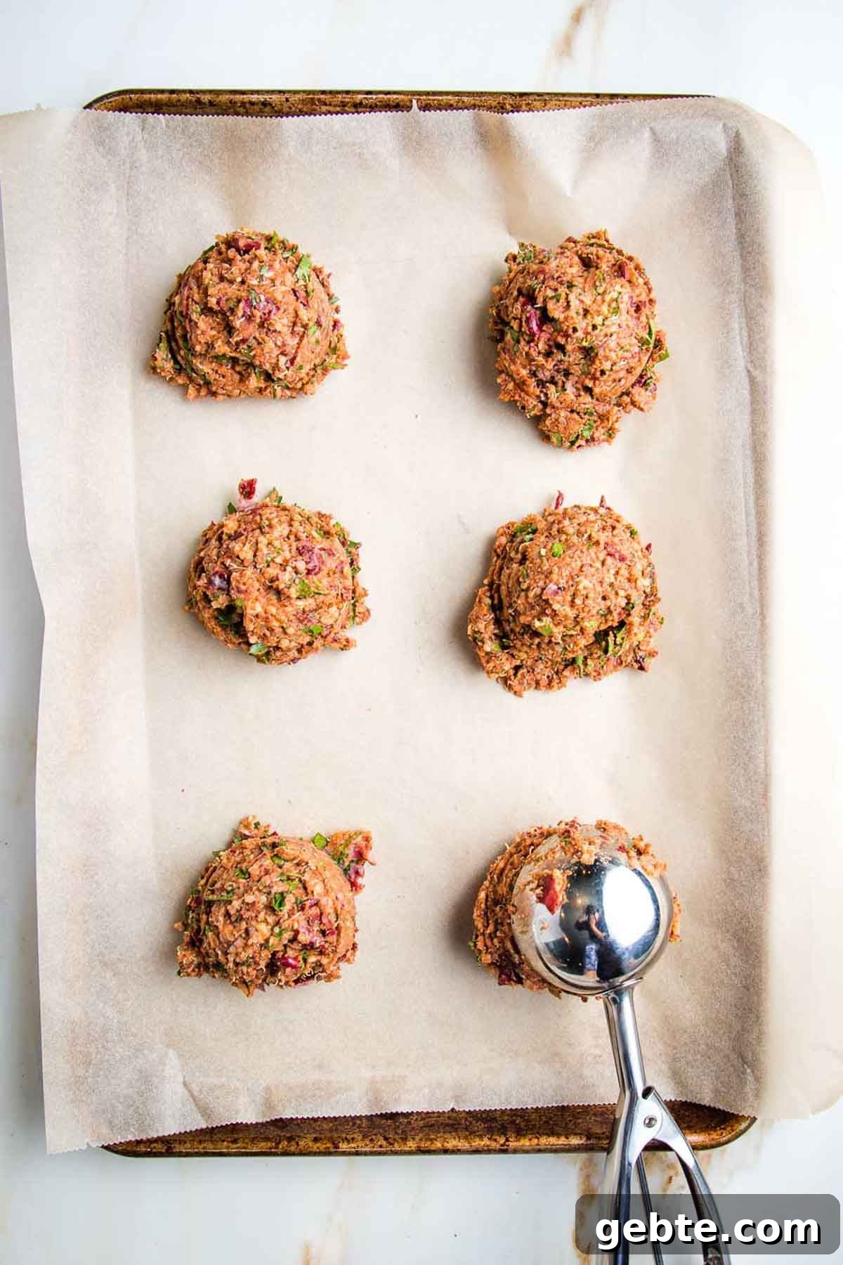 Portioning out veggie burgers onto a parchment lined baking sheet with a large scooper.