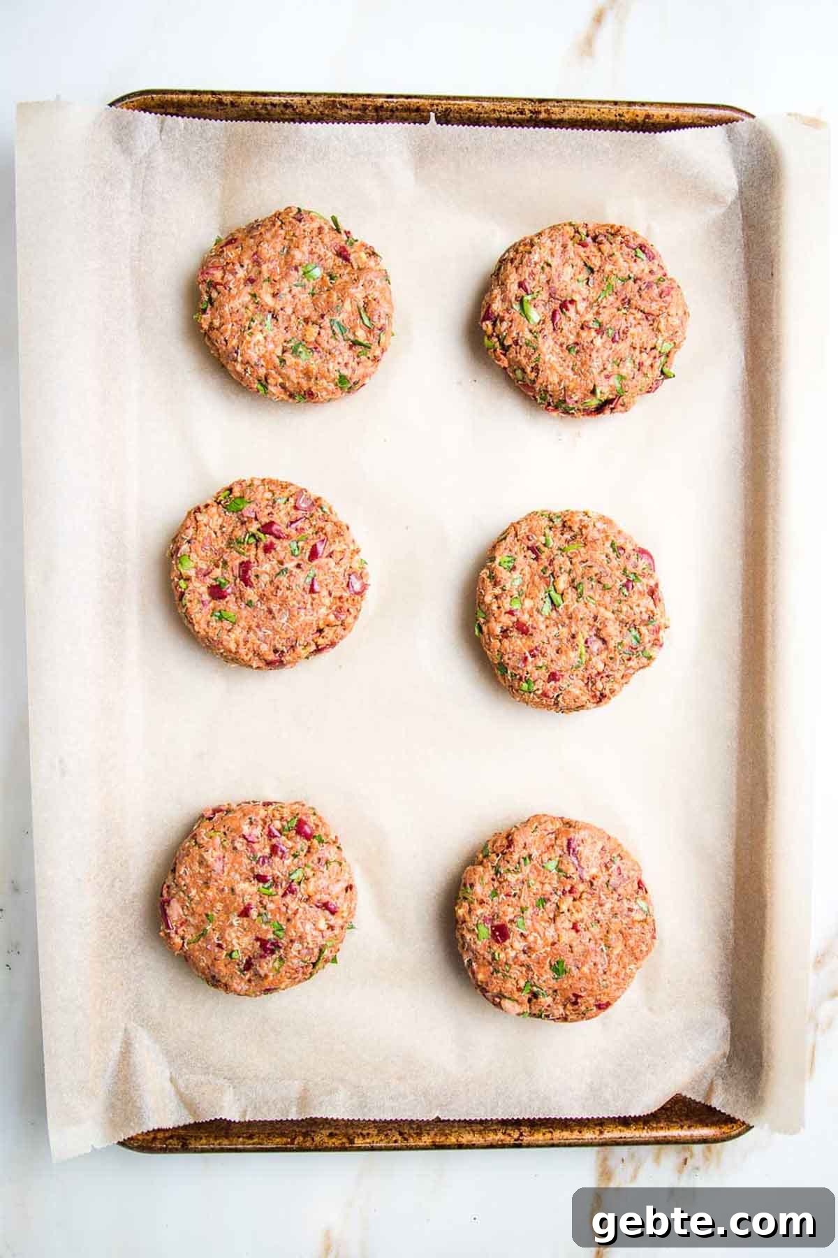 Six veggie burger patties on a parchment lined baking sheet.