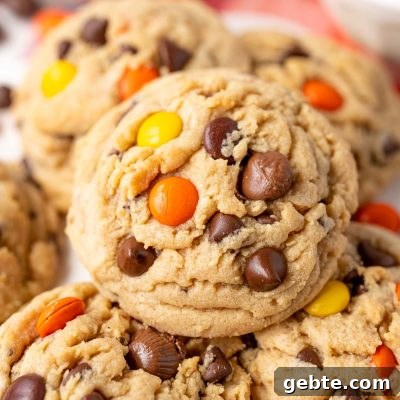 Close up of a peanut butter reese's pieces chocolate chip cookie on more cookies.