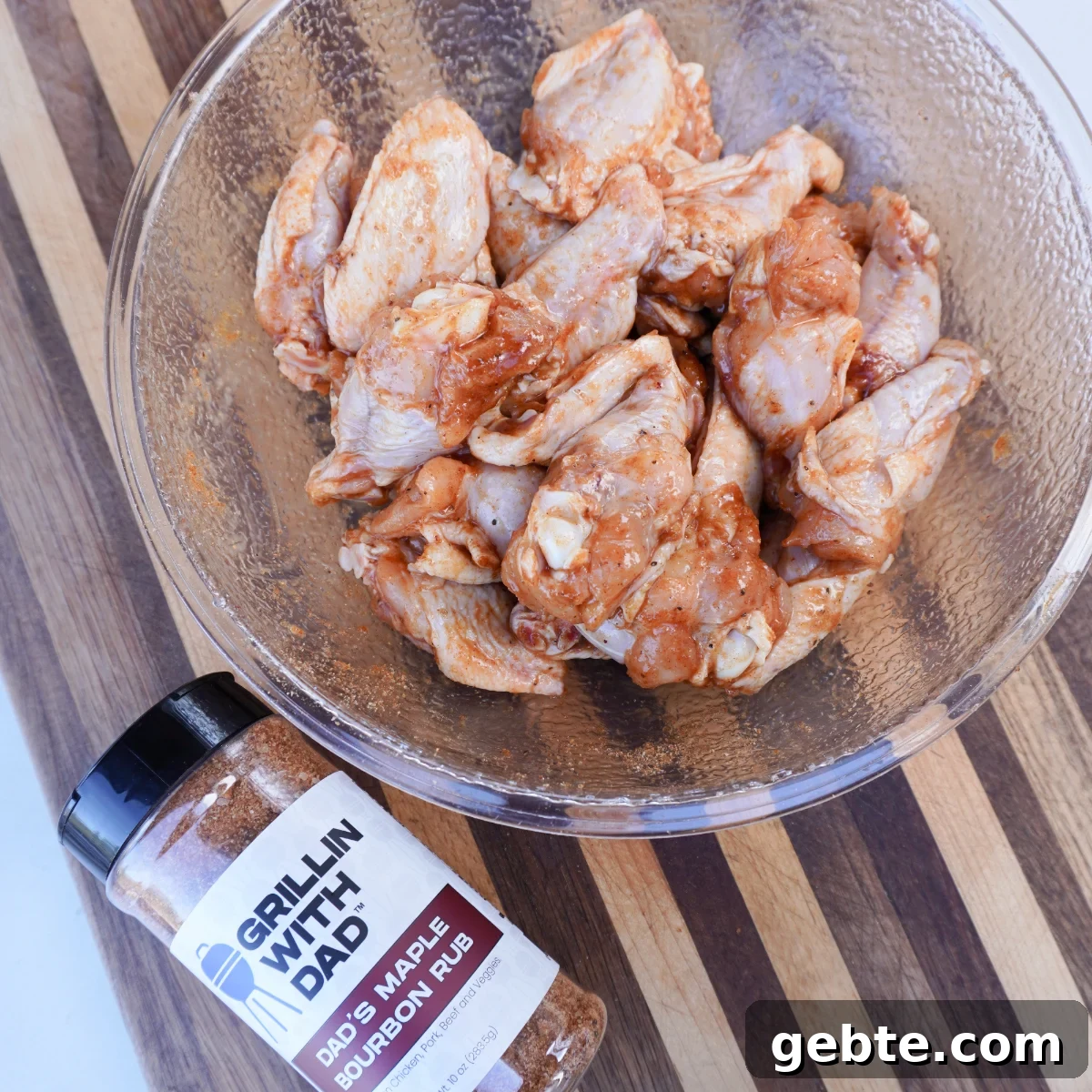 seasoned raw chicken wings in a clear bowl with a bottle of maple bourbon seasoning next to it.