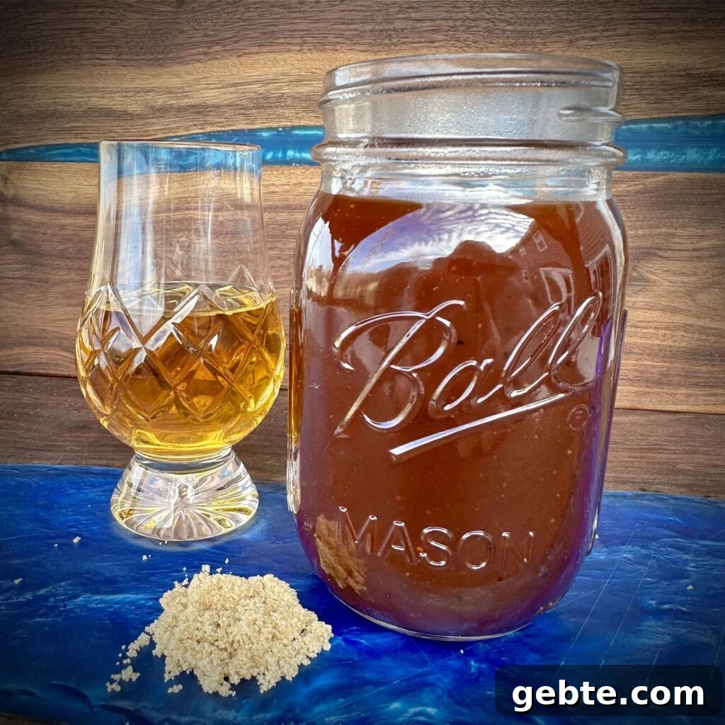 bourbon bbq sauce in a mason jar with a glass of bourbon and a pile of brown sugar.