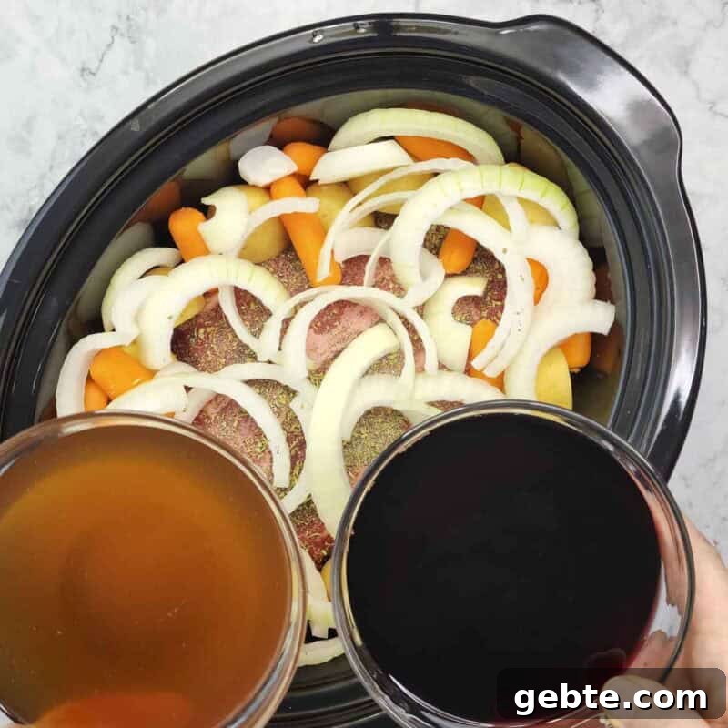 Add the sliced onion, potato halves, and carrots around and on top of the roast and pour the red wine and beef broth into the slow cooker.