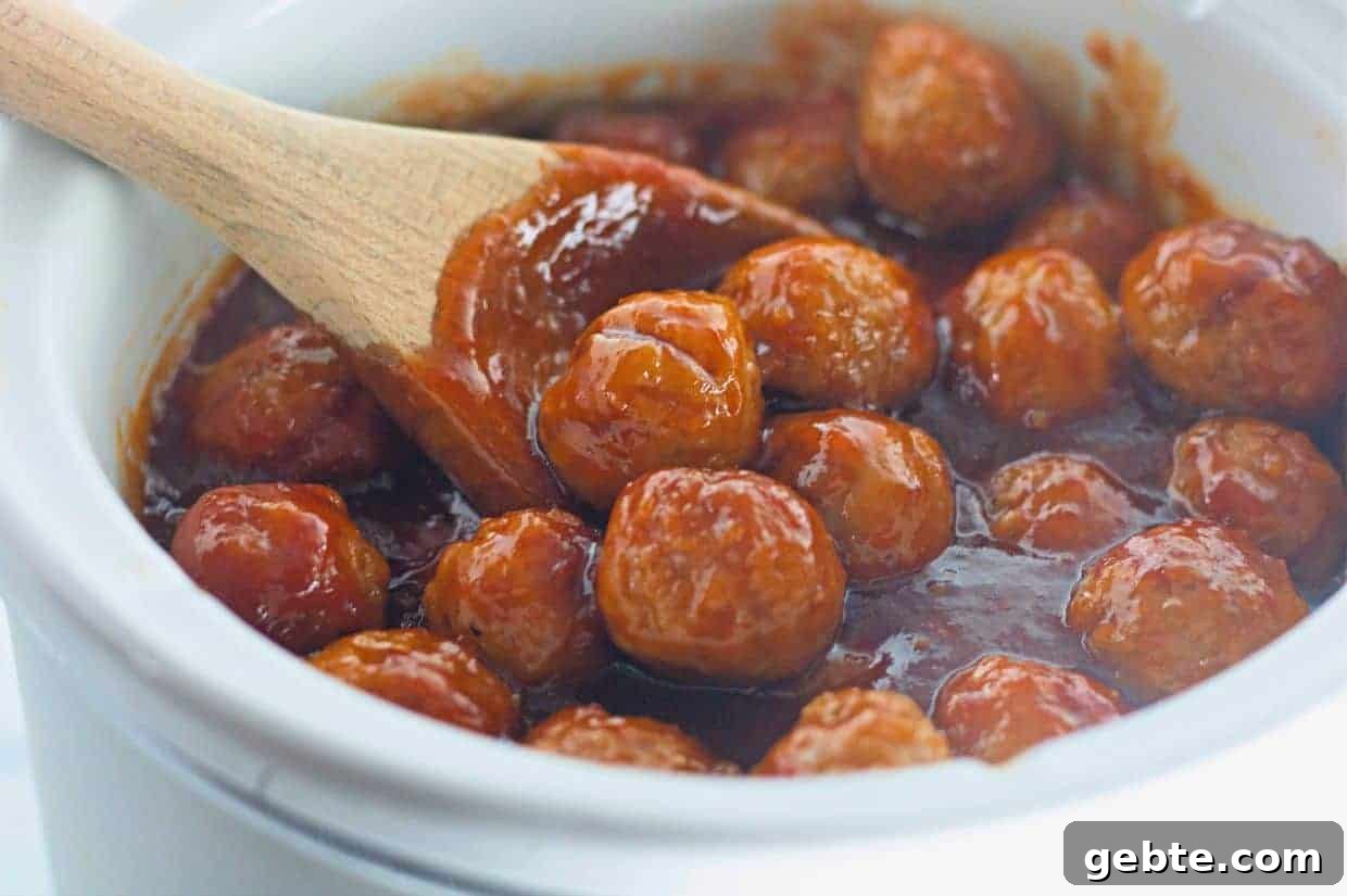 31 Slow Cooker Recipes to Walk In and Find Dinner Waiting 11 Honey-Garlic Meatballs in a thick red sauce are being stirred with a wooden spoon in a white ceramic pot.
