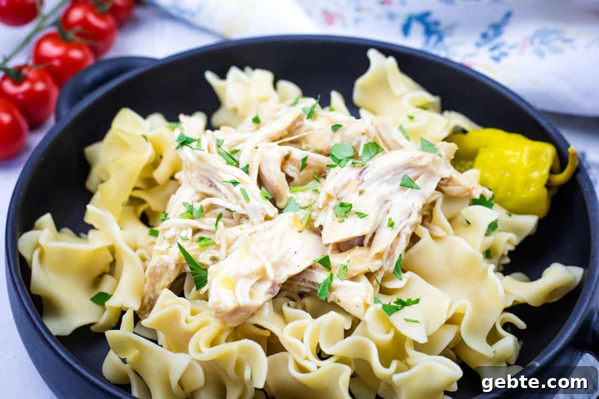 31 Slow Cooker Recipes to Walk In and Find Dinner Waiting 12 A black bowl containing egg noodles topped with Slow Cooker Mississippi Chicken and garnished with parsley, accompanied by a pickled pepper.