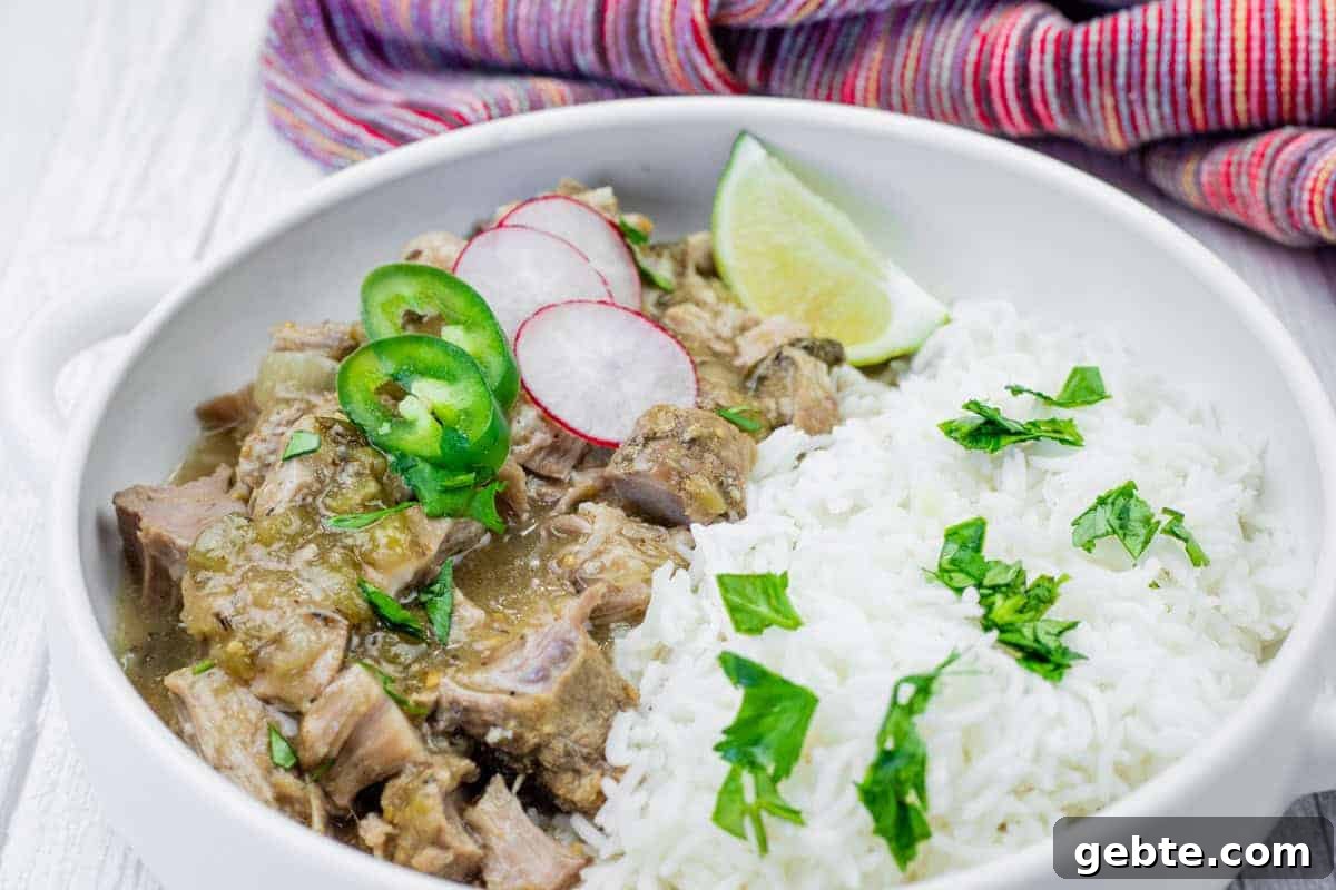 31 Slow Cooker Recipes to Walk In and Find Dinner Waiting 13 A bowl of white rice and green chili verde garnished with cilantro, radish slices, jalapeño, and a lime wedge, set on a white surface with a colorful cloth in the background.