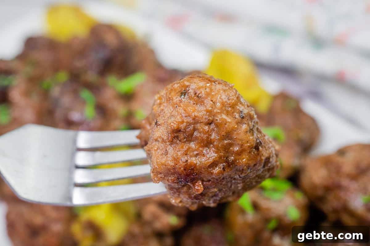 31 Slow Cooker Recipes to Walk In and Find Dinner Waiting 24 A close-up of a meatball on a fork, with more meatballs in the background.