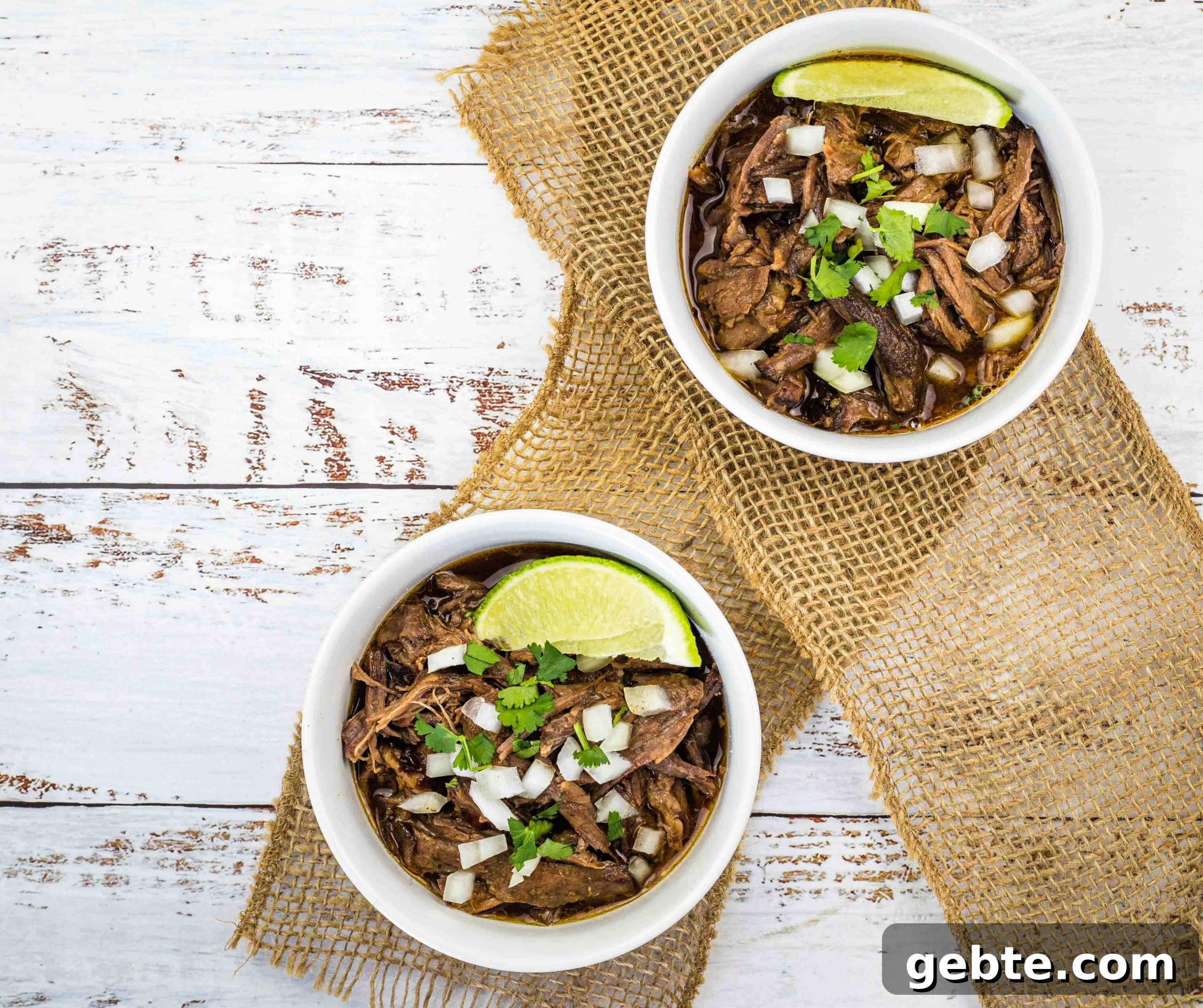 31 Slow Cooker Recipes to Walk In and Find Dinner Waiting 25 Two white bowls filled with slow cooker birria garnished with fresh lime wedges.