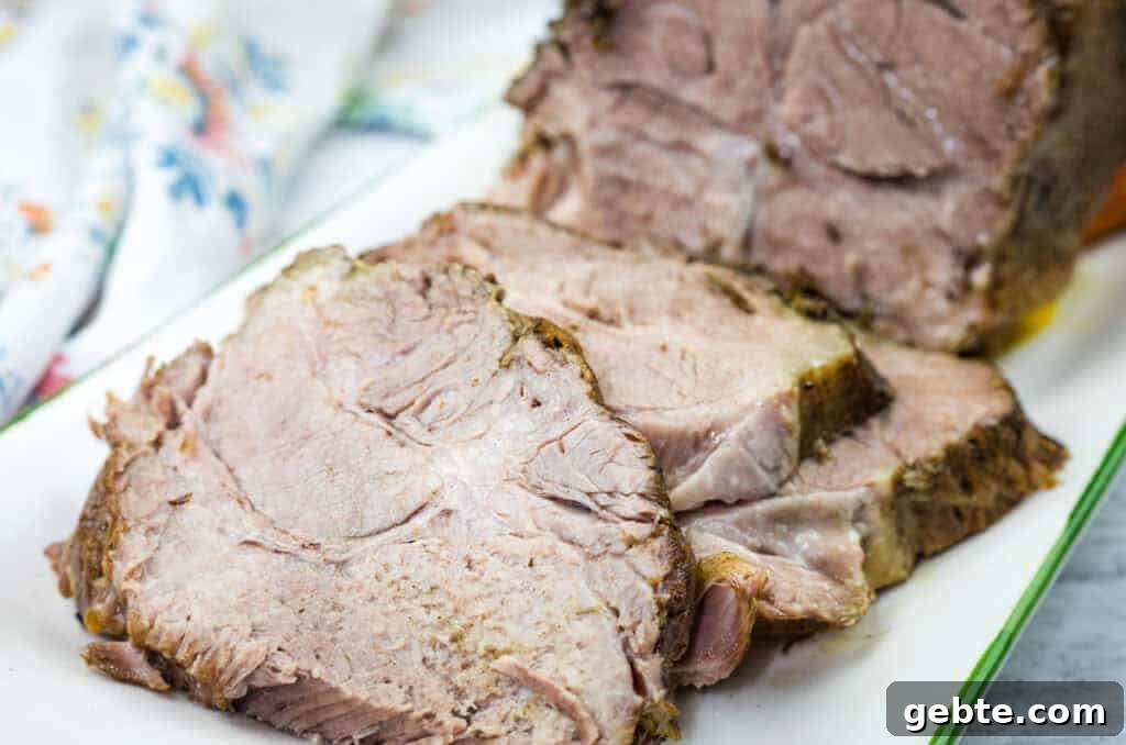 31 Slow Cooker Recipes to Walk In and Find Dinner Waiting 9 Sliced Herb-Crusted Pork Roast on a rectangular white plate with a floral napkin in the background.