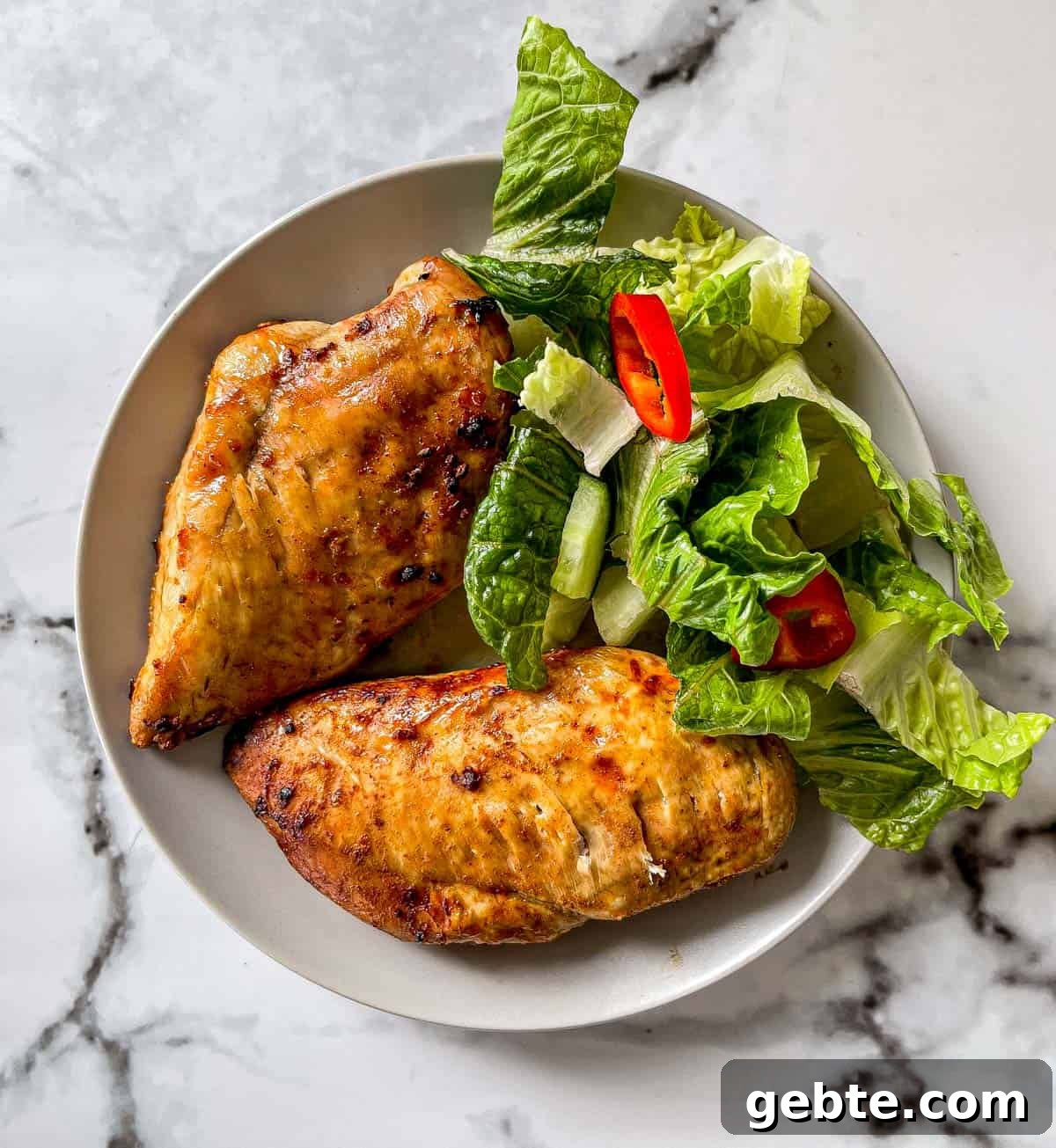 Juice air fried chicken breasts on a dinner plate with a green salad.