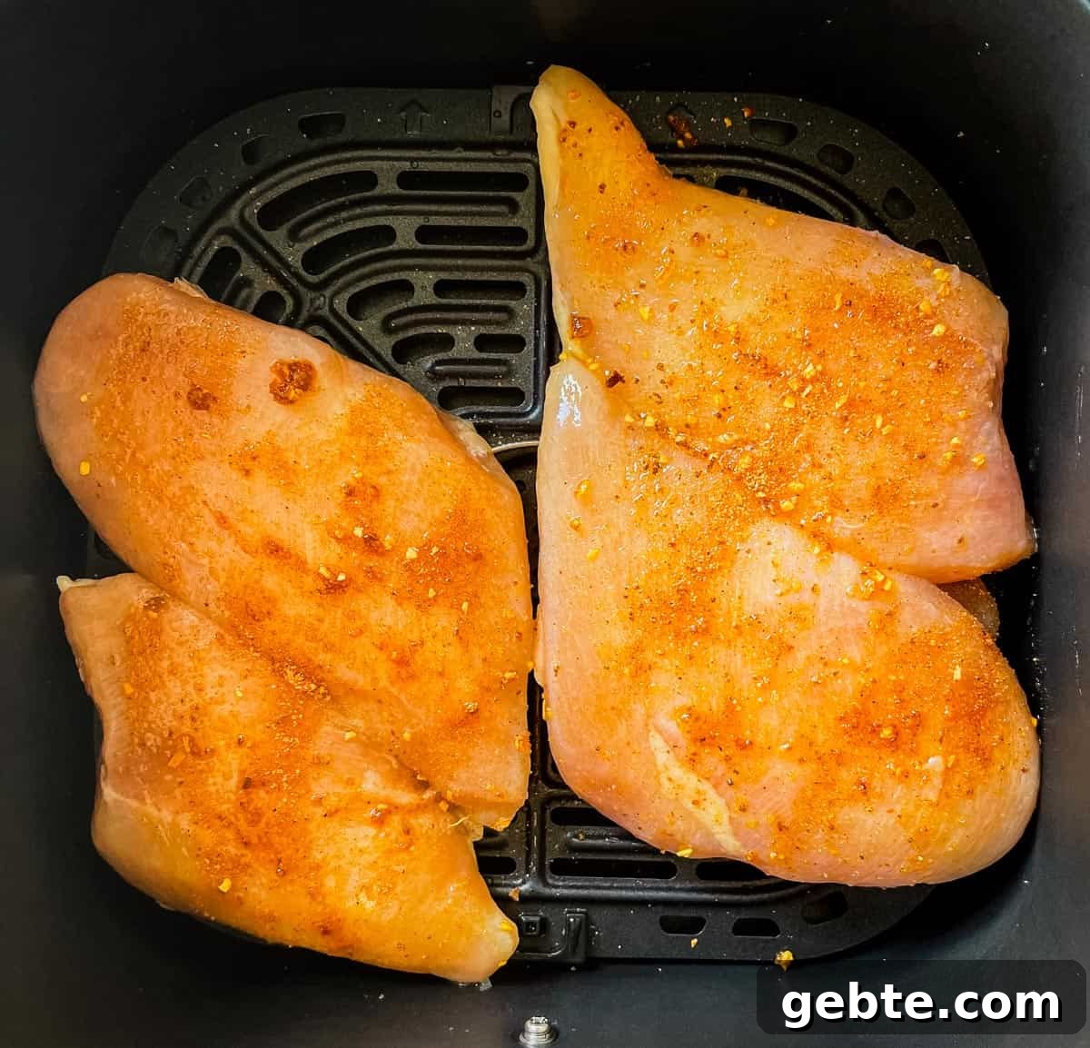 Frozen chicken breasts covered in rub and placed in the air fryer basket.