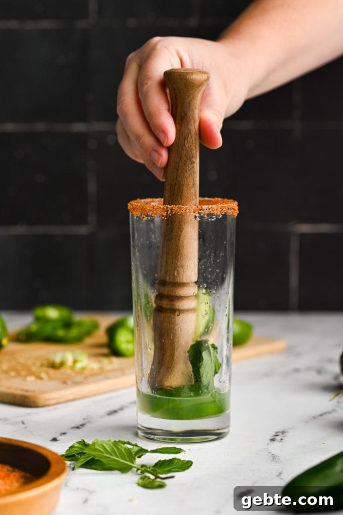 Using a wooden muddler to crush jalapenos and mint to extract flavor.