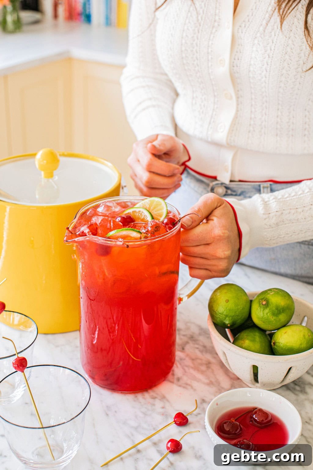 elizabeth holding a pitcher of dirty shirleys with an ice bucket, limes, and extra cherries on the side