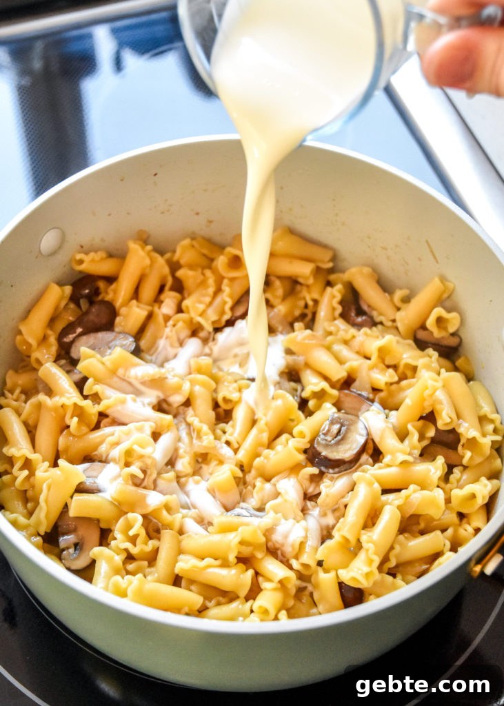 pouring heavy cream into a pot of cooked mushroom pasta.