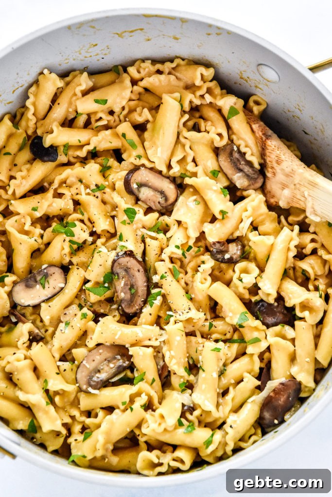 one pot creamy mushroom pasta with parmesan and parsley on top and wooden spoon in the pot.