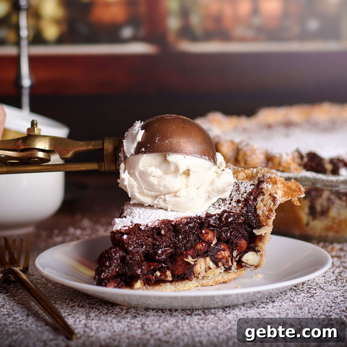 Decadent Chocolate Almond Pie Recipe — Crispy Crust & Rich Filling 14 Someone using an old fashioned ice cream scoop to top a slice of chocolate almond pie with a scoop of vanilla ice cream.