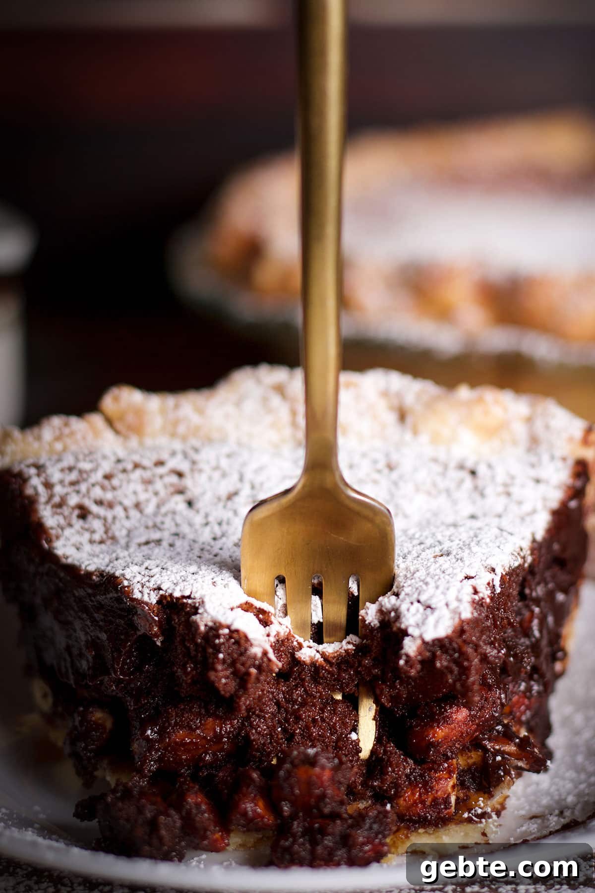 Decadent Chocolate Almond Pie Recipe — Crispy Crust & Rich Filling 15 Someone using a fork to cut a bite of chocolate almond pie from a slice on a white plate.