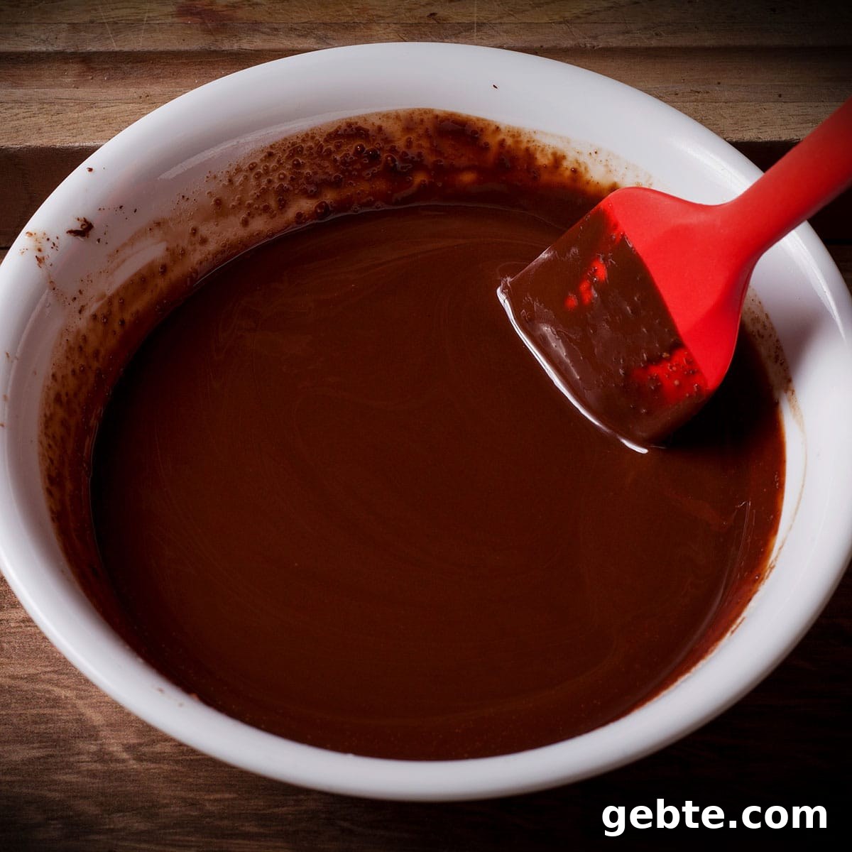 Decadent Chocolate Almond Pie Recipe — Crispy Crust & Rich Filling 7 Using a red spatula to stir melted chocolate with melted butter in a white bowl.