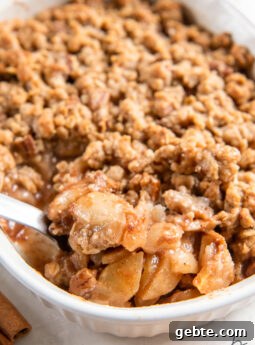 serving spoon lifting scoop of apple pear crisp from a baking dish.