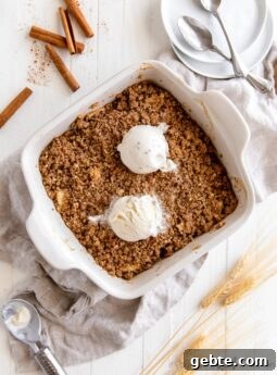 apple crisp in square ceramic baking dish with two scoops of vanilla ice cream on top
