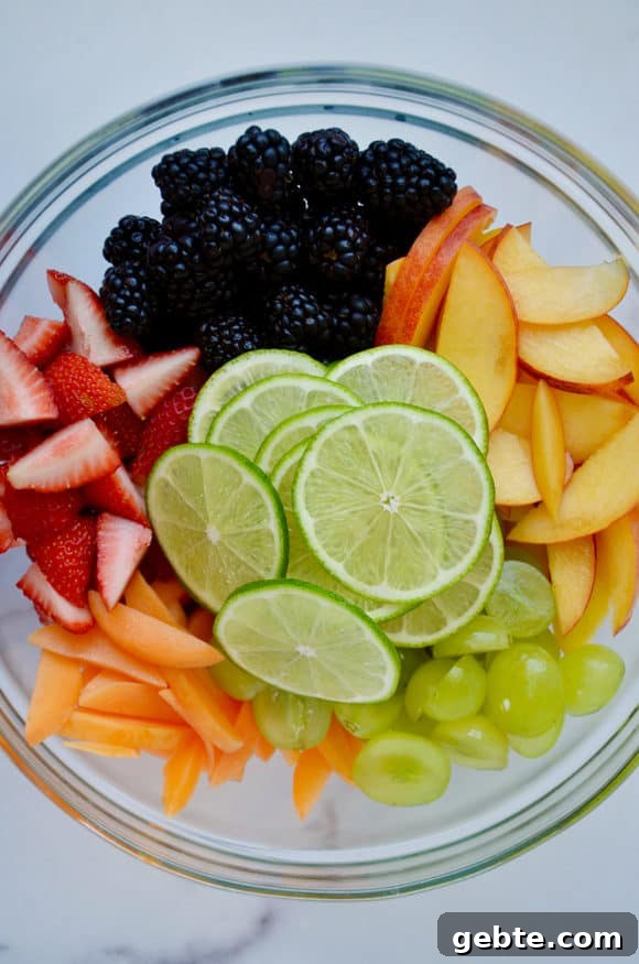Glass bowl with sliced limes, blackberries, apples, grapes, peaches and strawberries