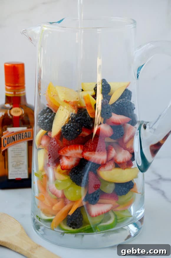 Pitcher containing chopped fresh fruit with orange liqueur in the background