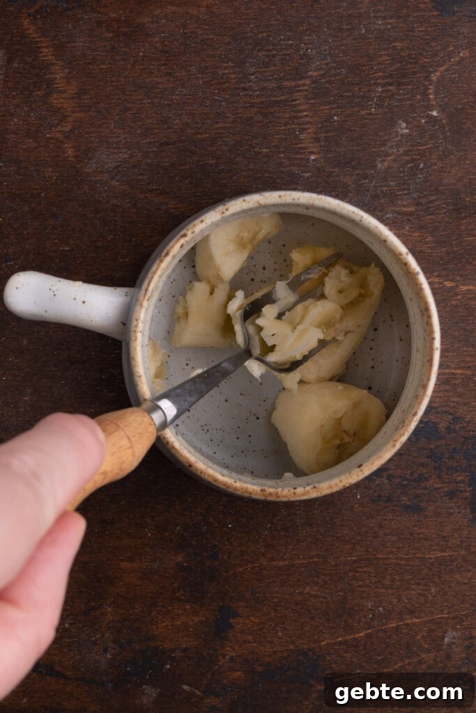 Using fork to smash a banana in a mug.