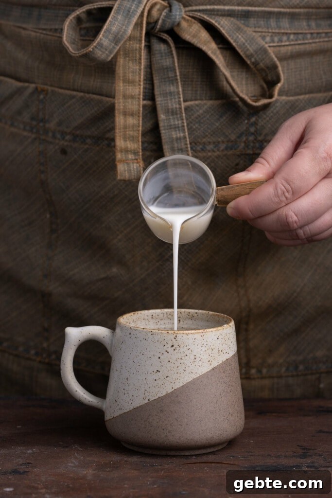 Adding milk to make banana batter in a mug.