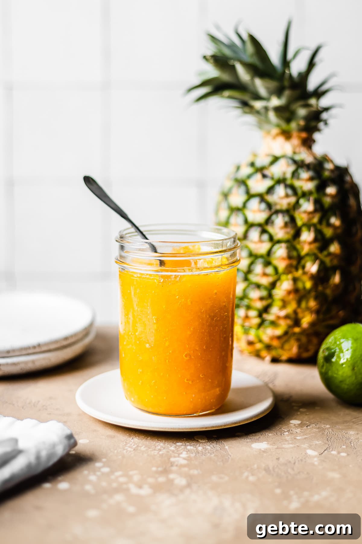A glass jar of pineapple jam with a spoon inside.