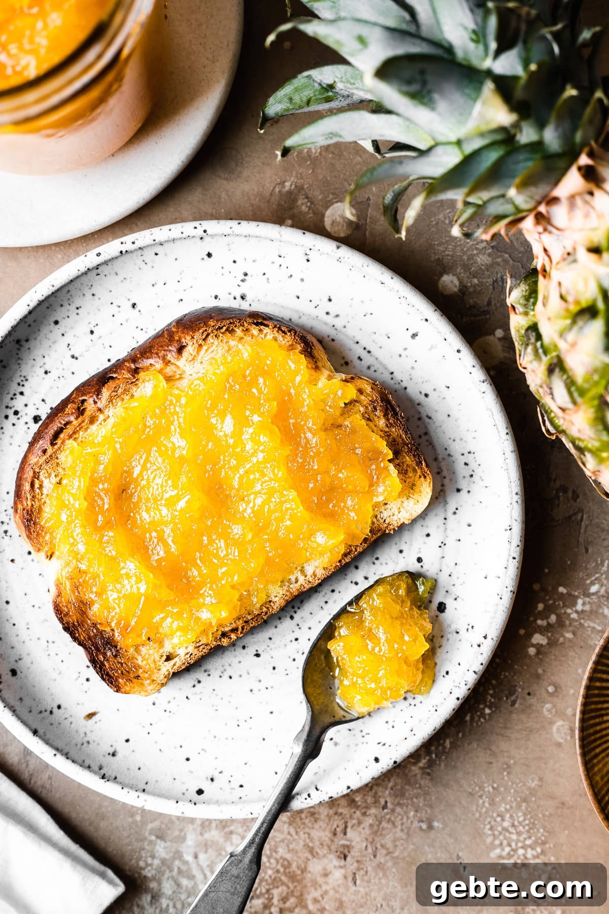 A piece of toast spread with bright yellow pineapple jam on a plate.