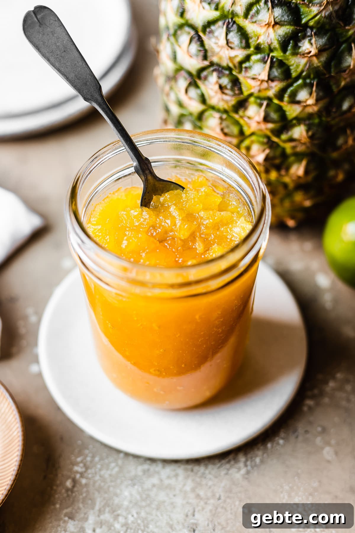 A glass jar of golden colored jam with a spoon inside.