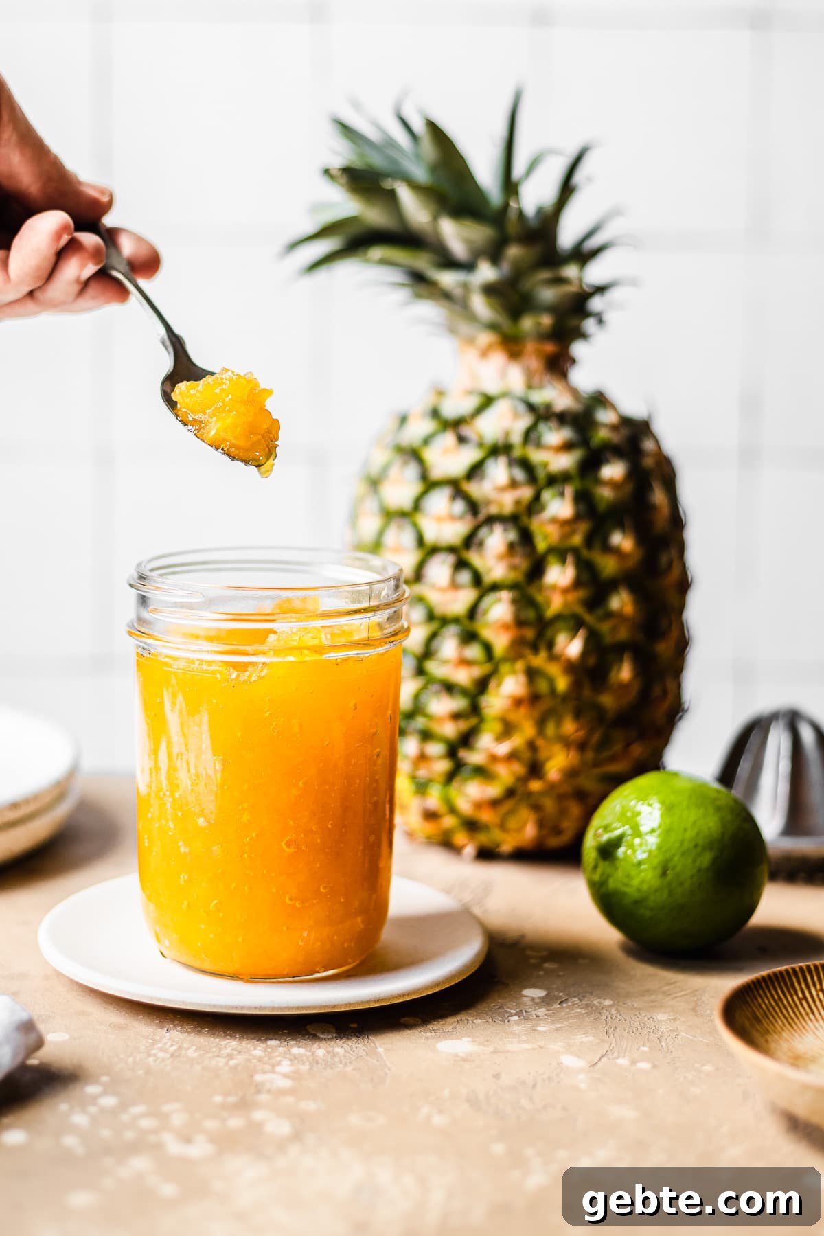 A jar of pineapple jam with a hand holding a jam filled spoon.